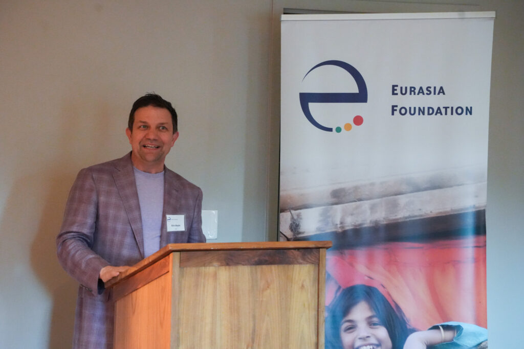 Eric Boyle, senior vice president at ICF, stands at a podium in front of a Eurasia Foundation banner to address fellows at the closing ceremony.