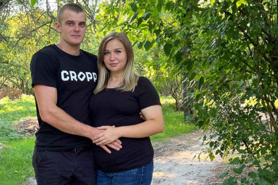 A photo shows Anhelina, a pregnant woman, and her partner standing outside with their arms around each other.