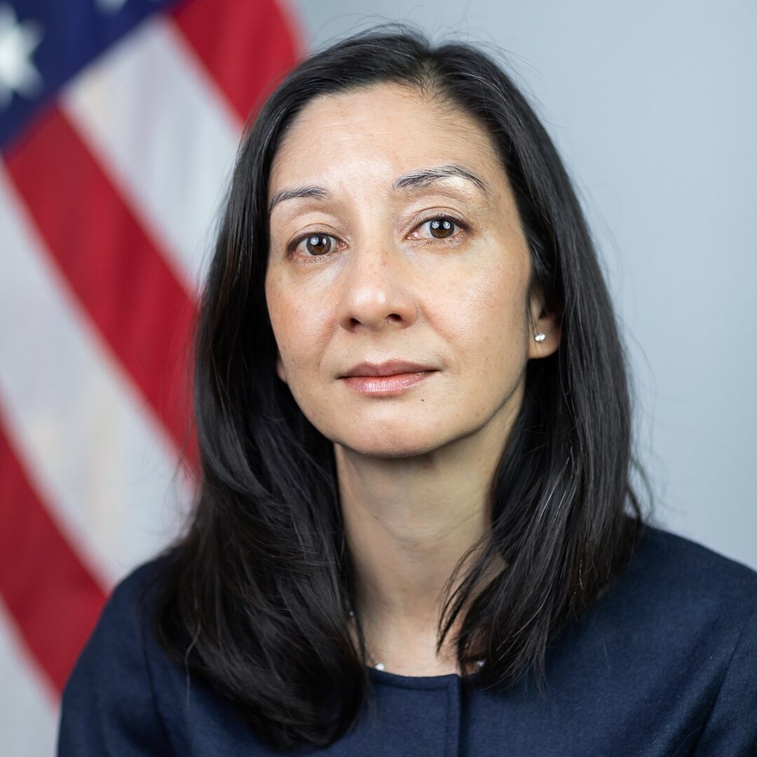 A headshot of Shanthi Kalathil in professional attire in front of an American flag